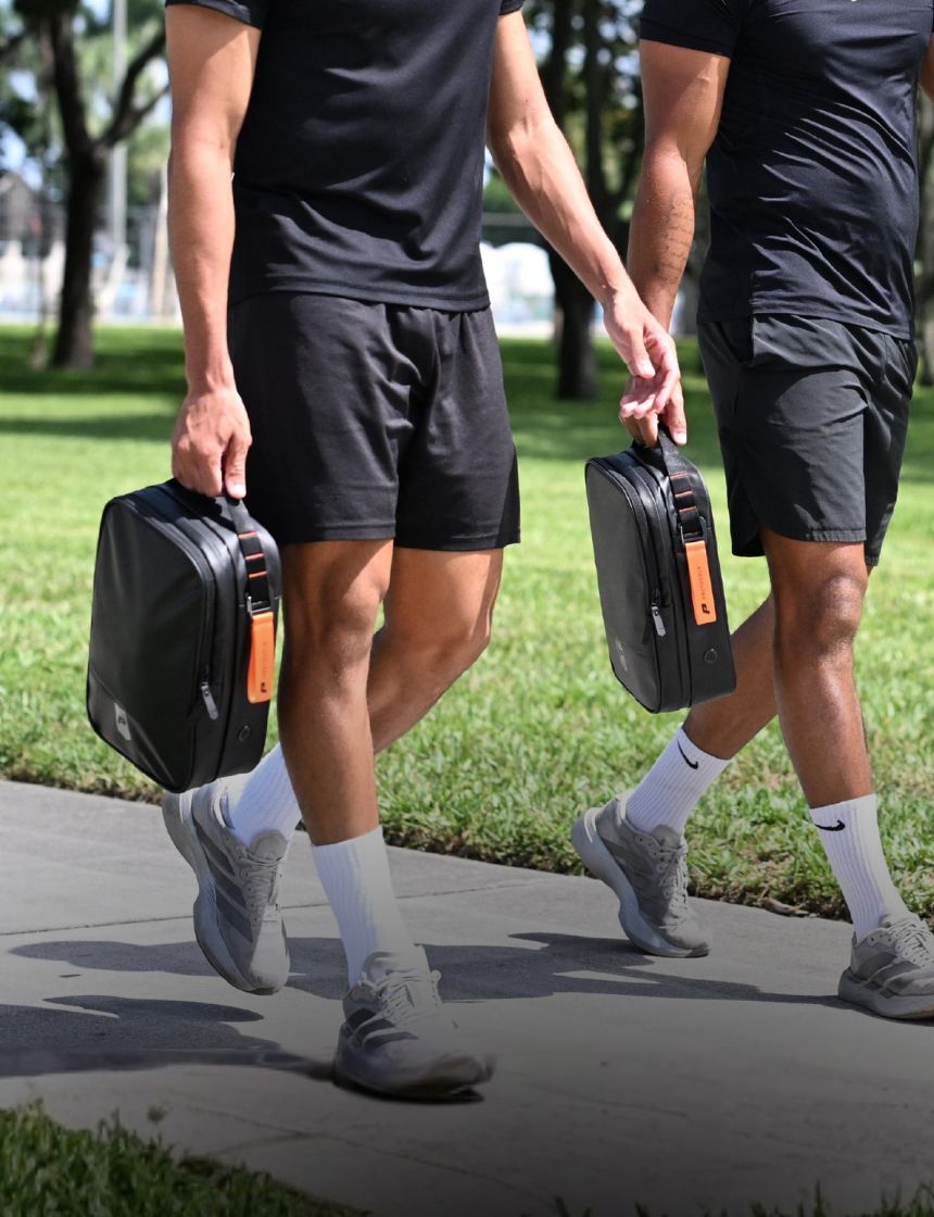 Two footballers carrying the Kinetic Boot Bag in black with orange zip pull, walking outdoors before training