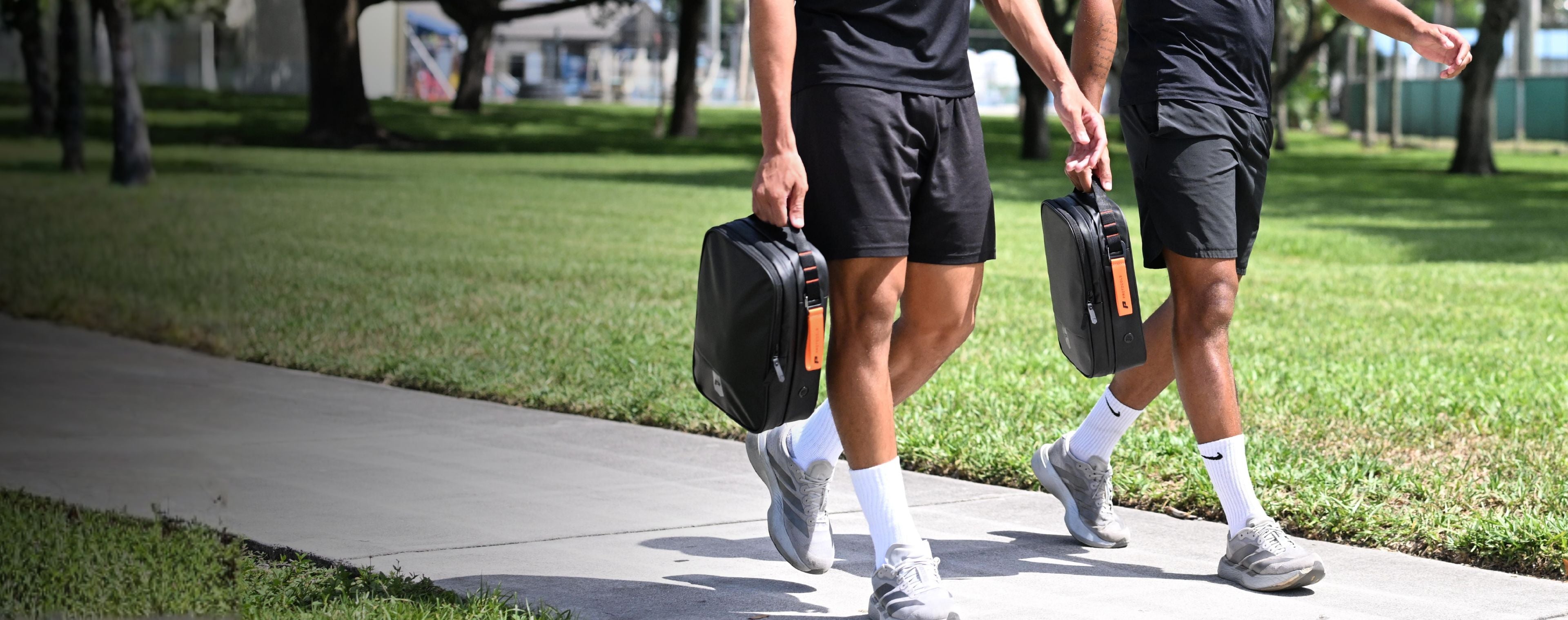 Two footballers carrying the Kinetic Boot Bag in black with orange zip pull, walking outdoors before training
